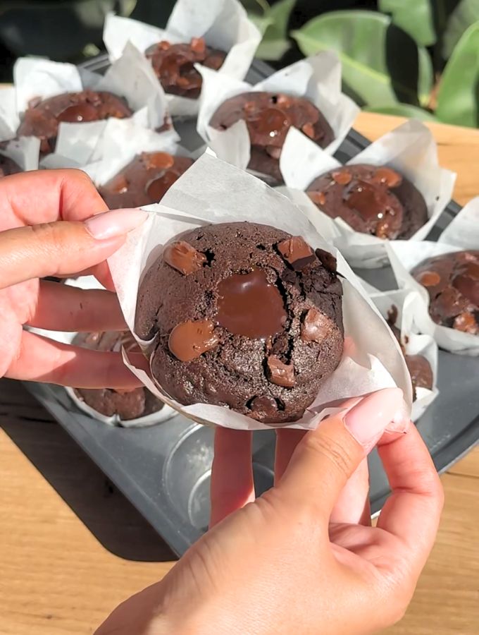 Hand holding a double chocolate muffin with the parchment paper liners.