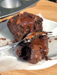 A silver fork cutting into a rich double chocolate muffin, revealing a core of warm, melting ganache.