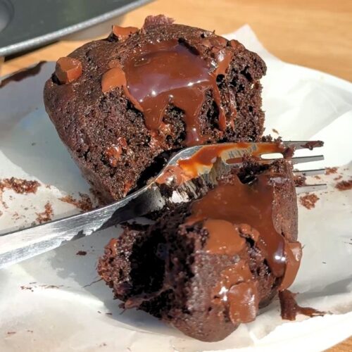 A silver fork cutting into a rich double chocolate muffin, revealing a core of warm, melting ganache.