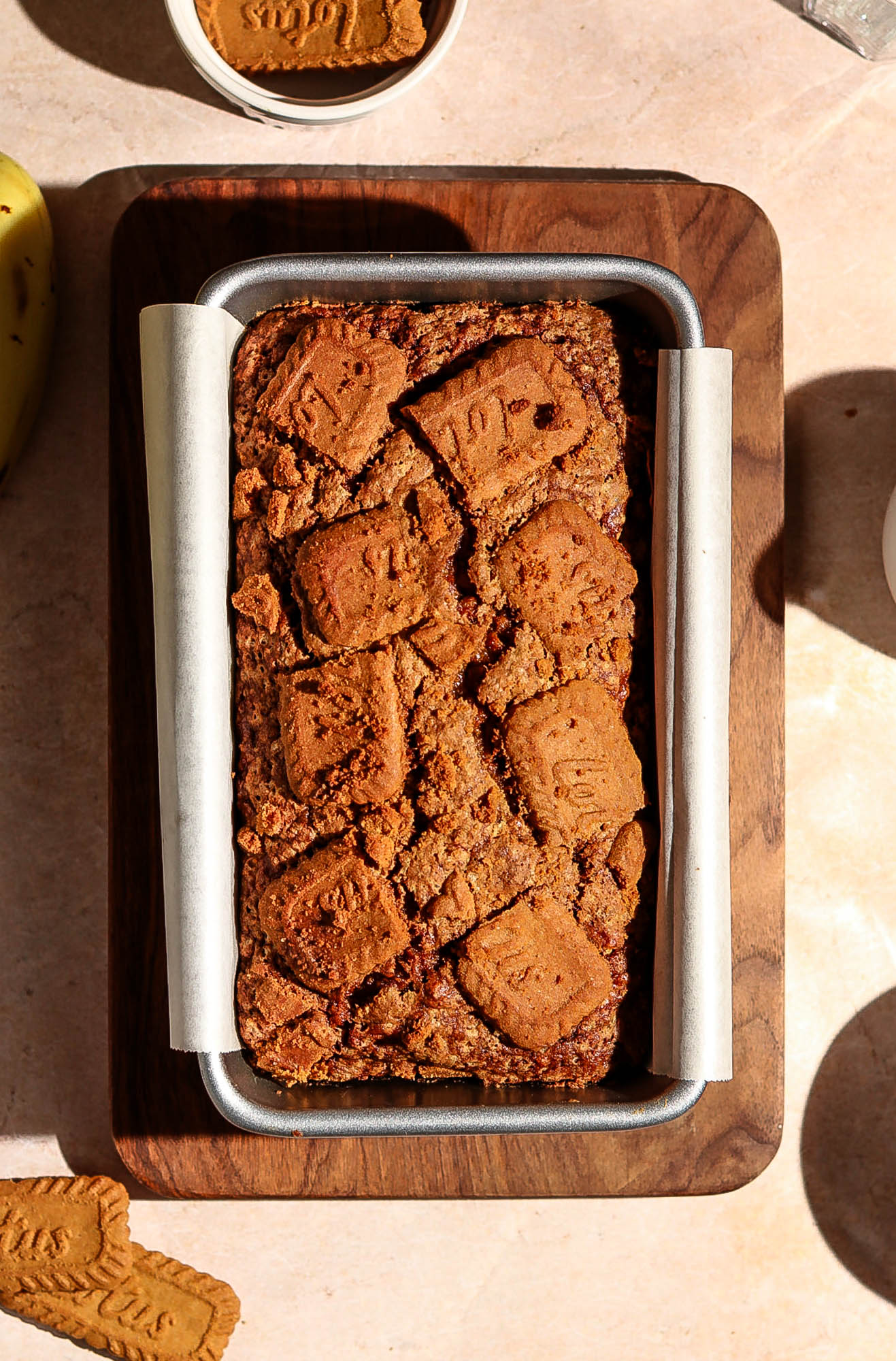 Top-down view of a freshly baked Biscoff banana bread in a loaf pan lined with parchment paper, topped with whole and broken Lotus Biscoff cookies.