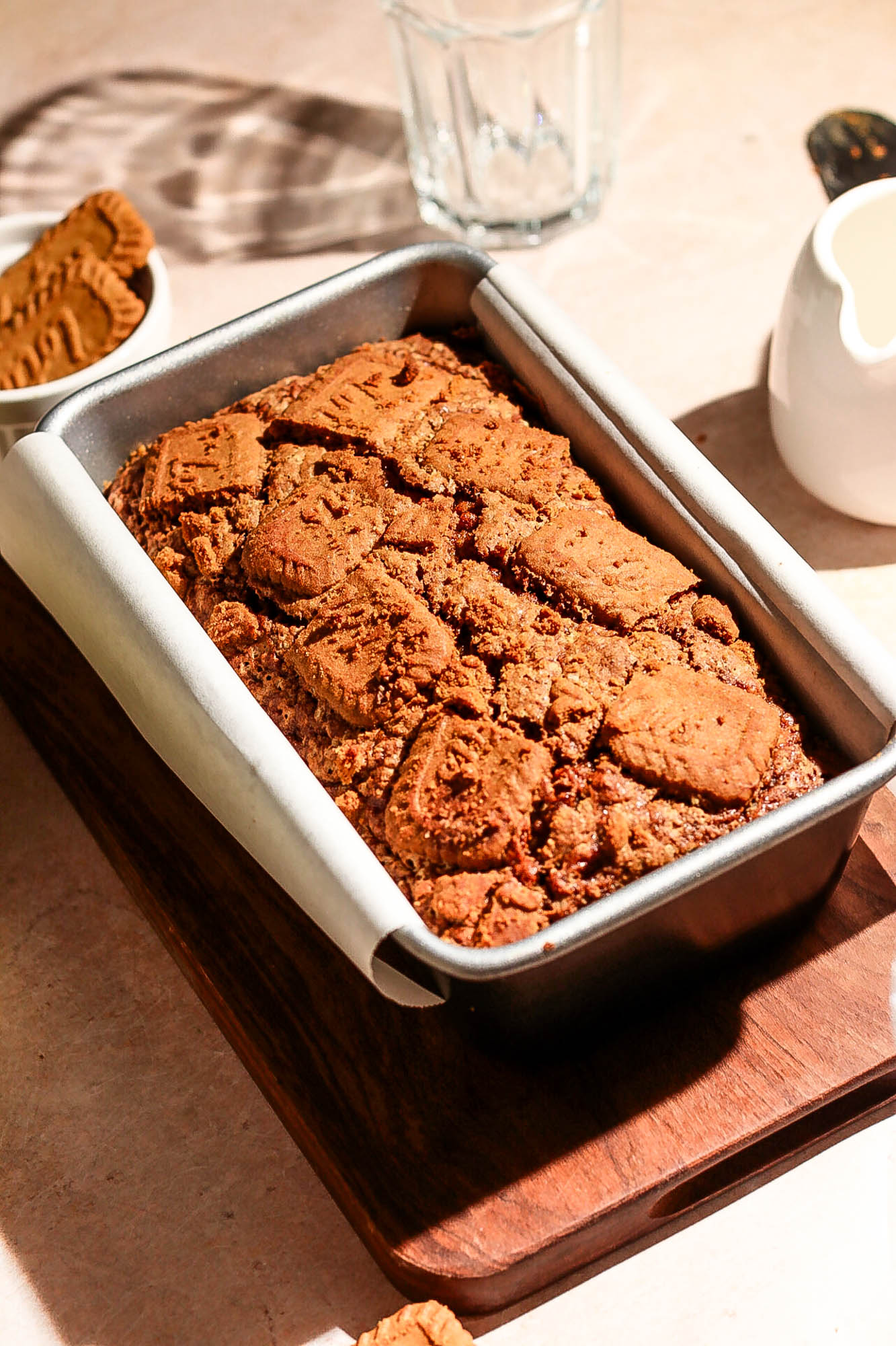 Angled view of a freshly baked Biscoff banana bread inside a loaf pan resting on a wooden board.