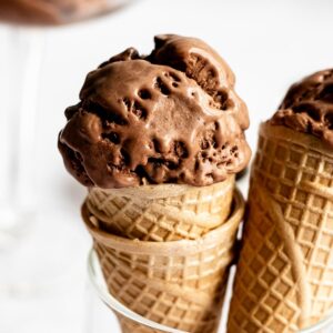 Two ice cream cones topped with chocolate ice cream.