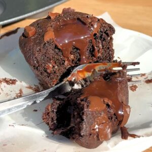 A silver fork cutting into a rich double chocolate muffin, revealing a core of warm, melting ganache.