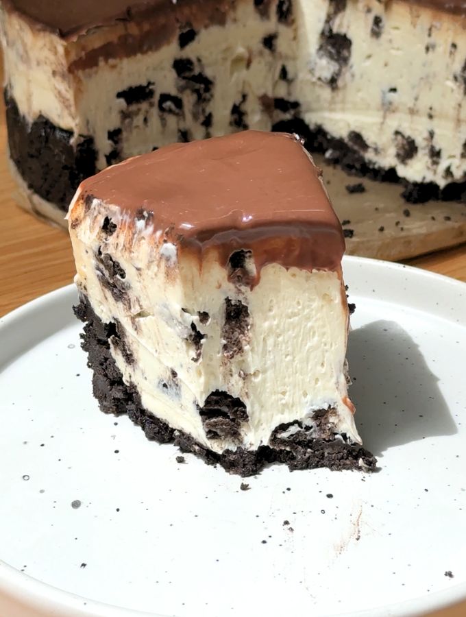 A close-up shot of a slice of Oreo cheesecake on a white dessert plate with one fork bite missing.