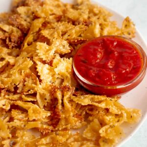 Pasta chips on a plate with tomato dip on the side.