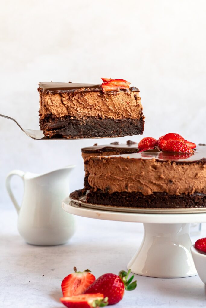 triple chocolate brownies mousse cake slice on a cake platter with strawberries on the side.