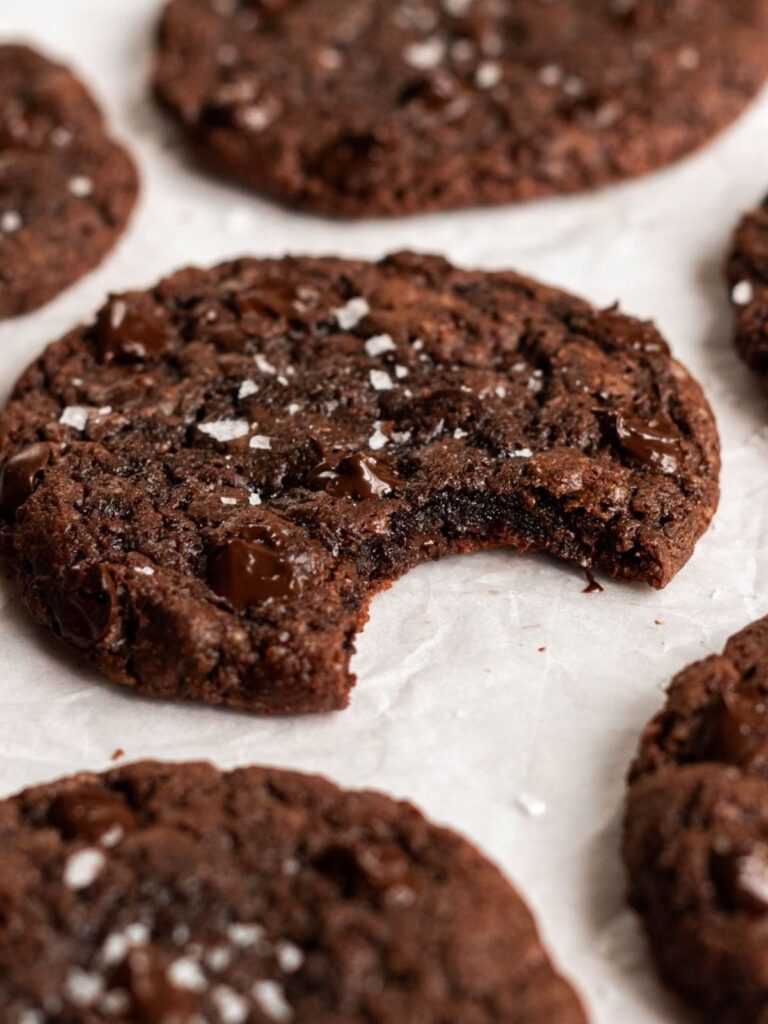 Bite missing from chocolate cookie on parchment paper.