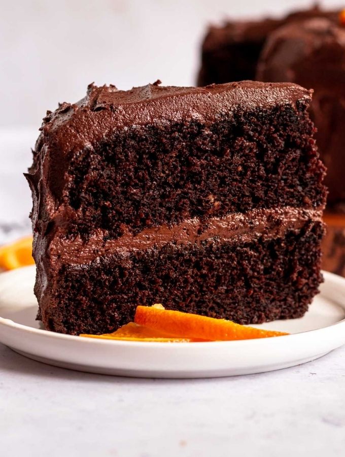 Slice of chocolate orange cake with a slice of orange on the side.