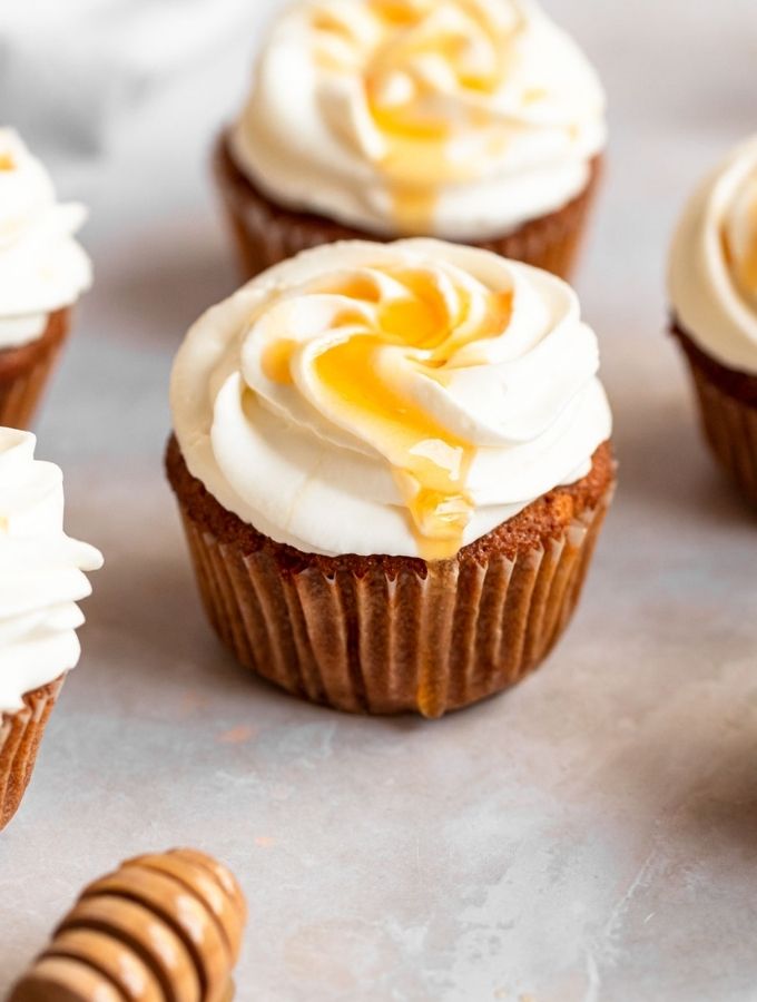 Honey cupcakes with whipped cream and honey on top.