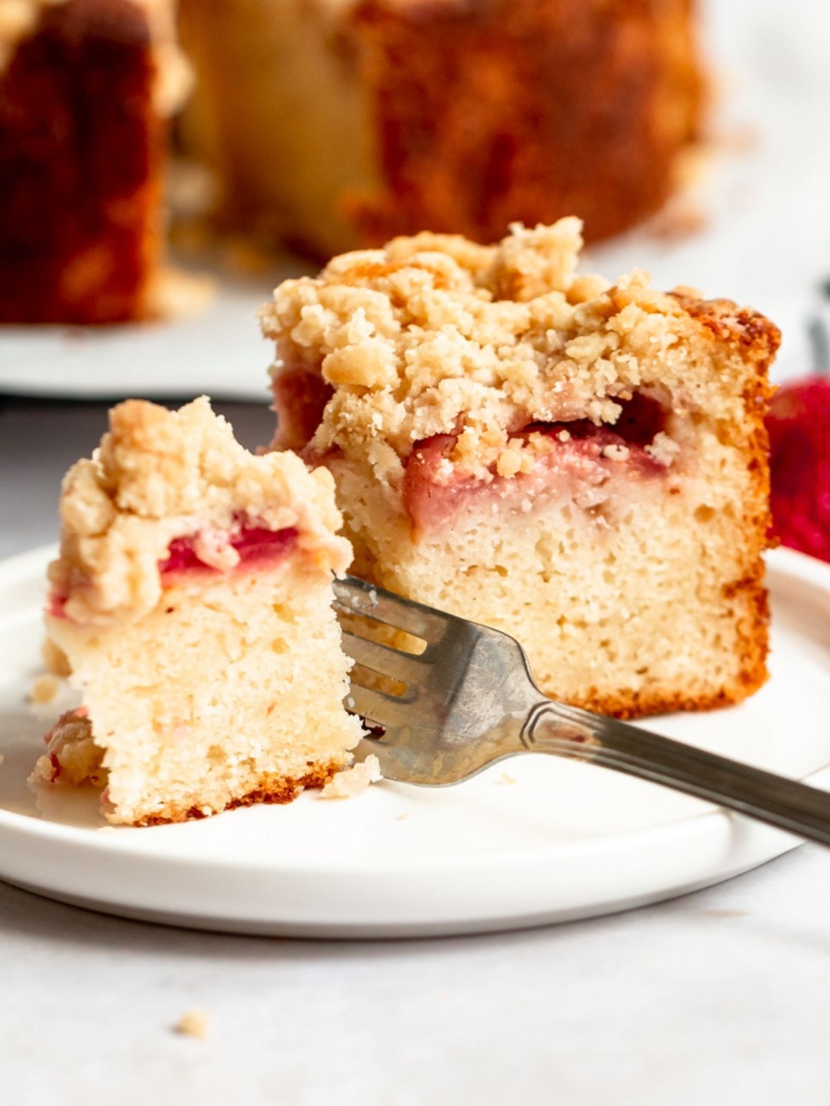 Strawberry crumble cake slice on a plate with a fork inserted into the slice.