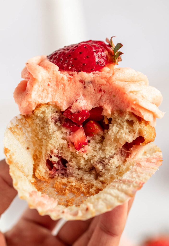 Hand holding an opened cupcake with strawberries on the inside.