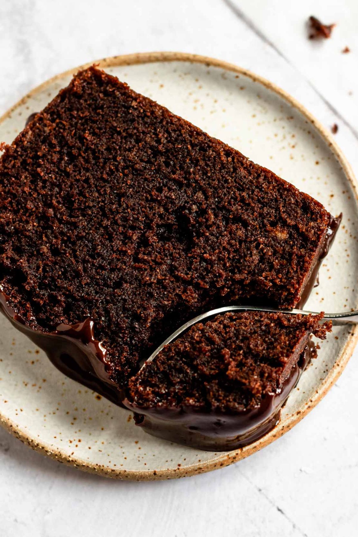 Top-down view of a single slice of moist chocolate sour cream pound cake with ganache on a plate, with a fork taking a bite.