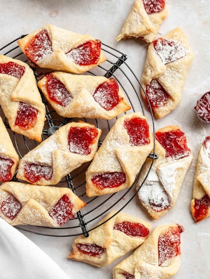 Kolaczki cookies with powder sugar on top on a round cooling rack.