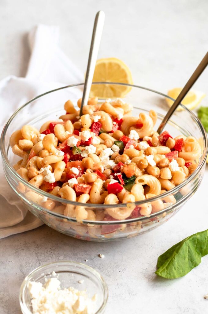 A big bowl of pasta salad with chickpeas and two spoons in the bowl.