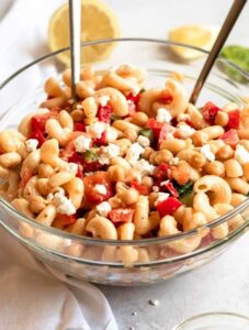 A big bowl of pasta salad with chickpeas and two spoons in the bowl.