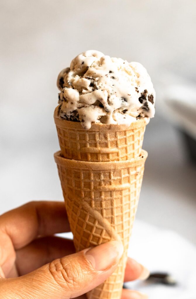 Hand holding an ice cream cone with oreo ice cream.