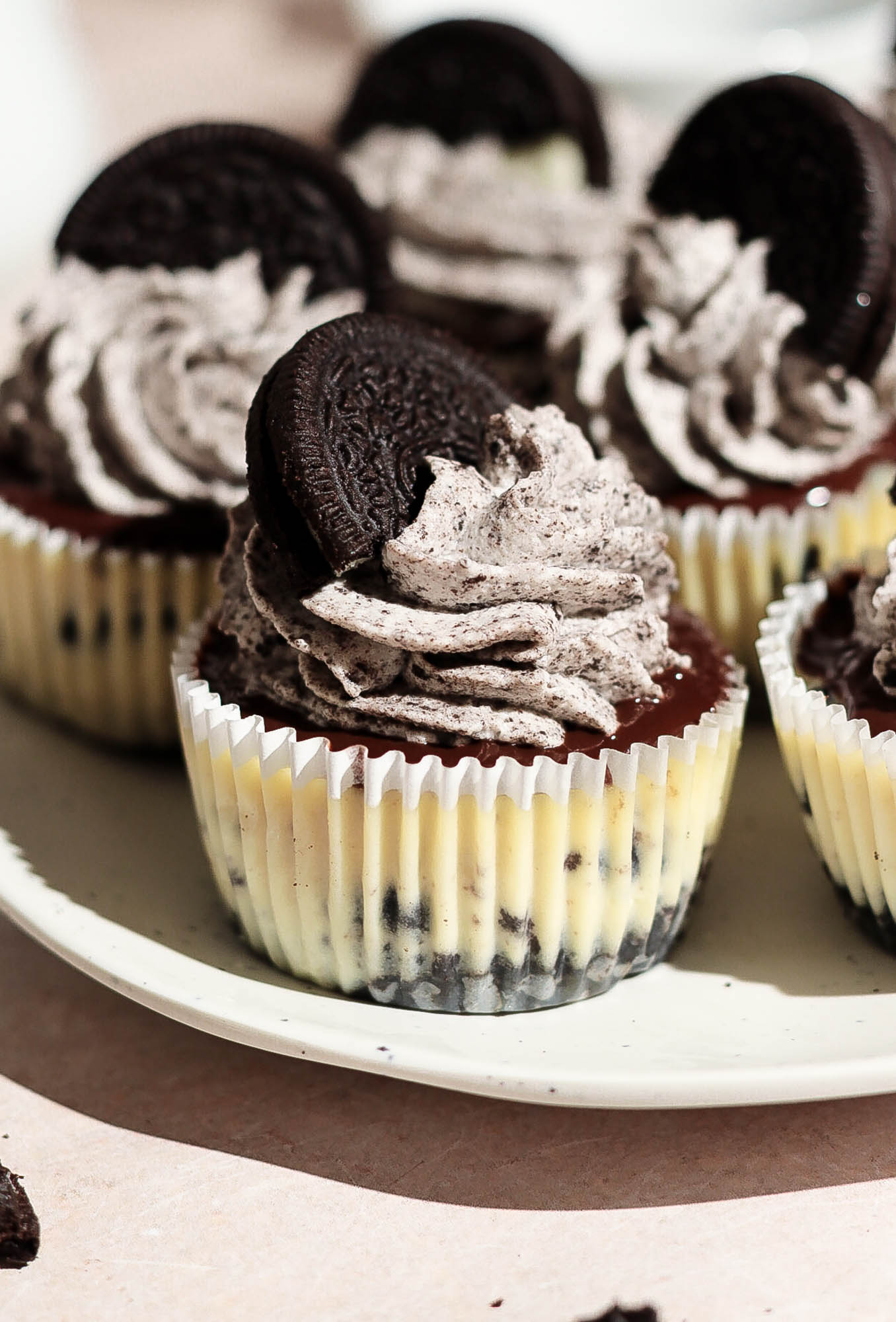 Close up of a single mini Oreo cheesecake showing the dark Oreo crust, creamy filling, chocolate ganache layer, and whipped cream swirl