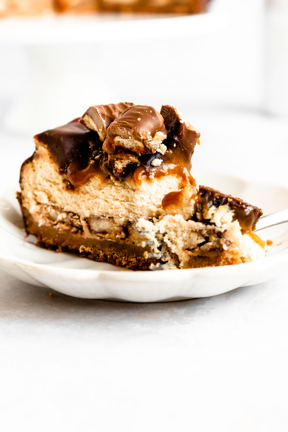 Slice of twix cheesecake on a white plate.