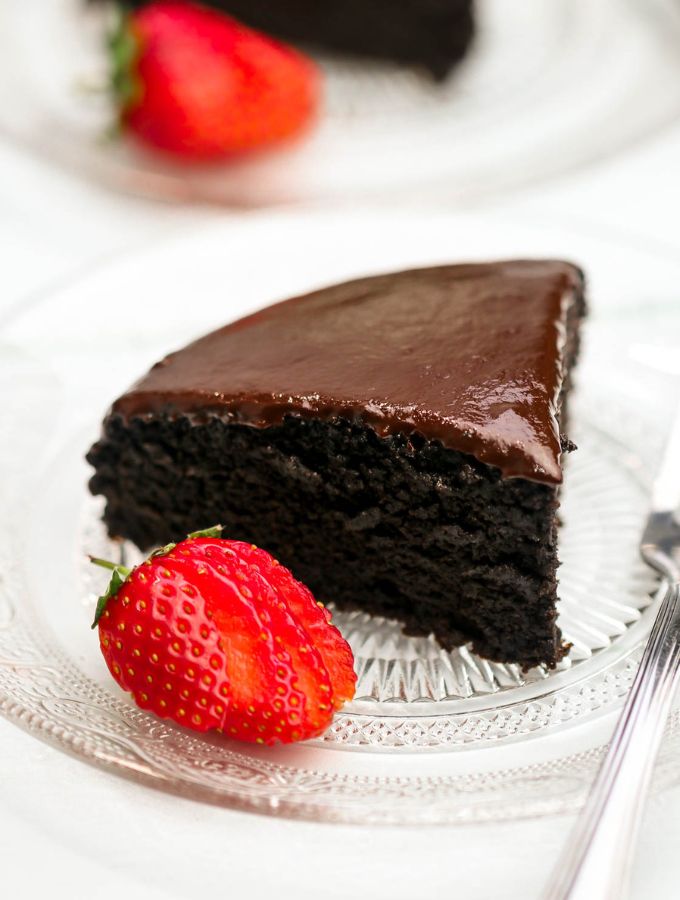 Slice of 3 ingredient chocolate cake on a small plate with a strawberry next to it.