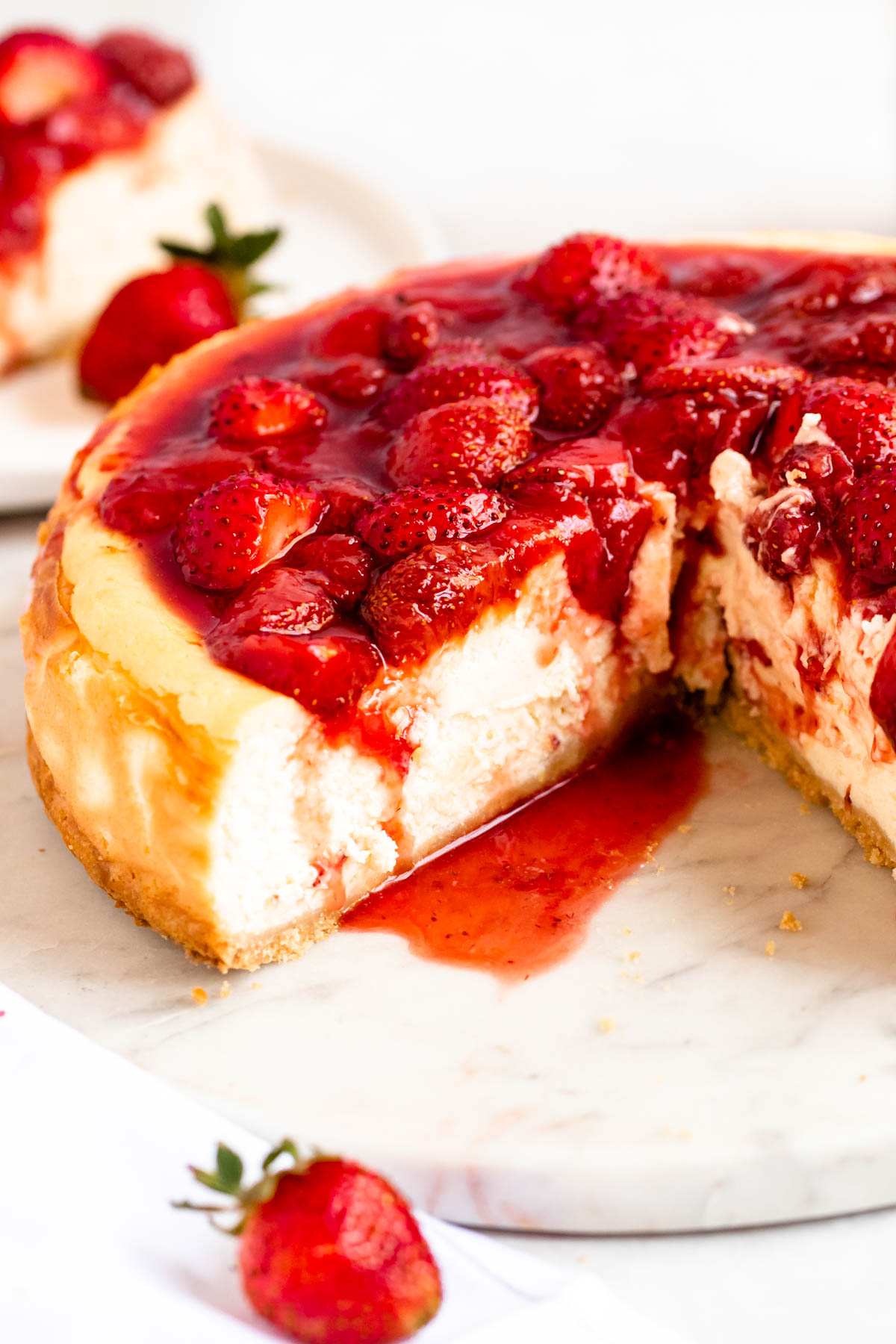 Slice missing from strawberry cheesecake with strawberry sauce.