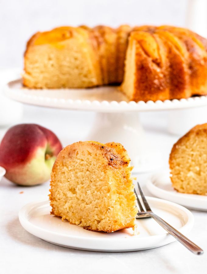 Slice of peach cobbler pound cake on a white plate next to the whole cake.