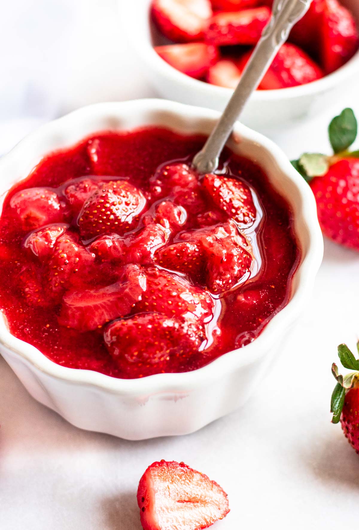 Close up shot of strawberry sauce in a white bowl with a spoon in the bowl.