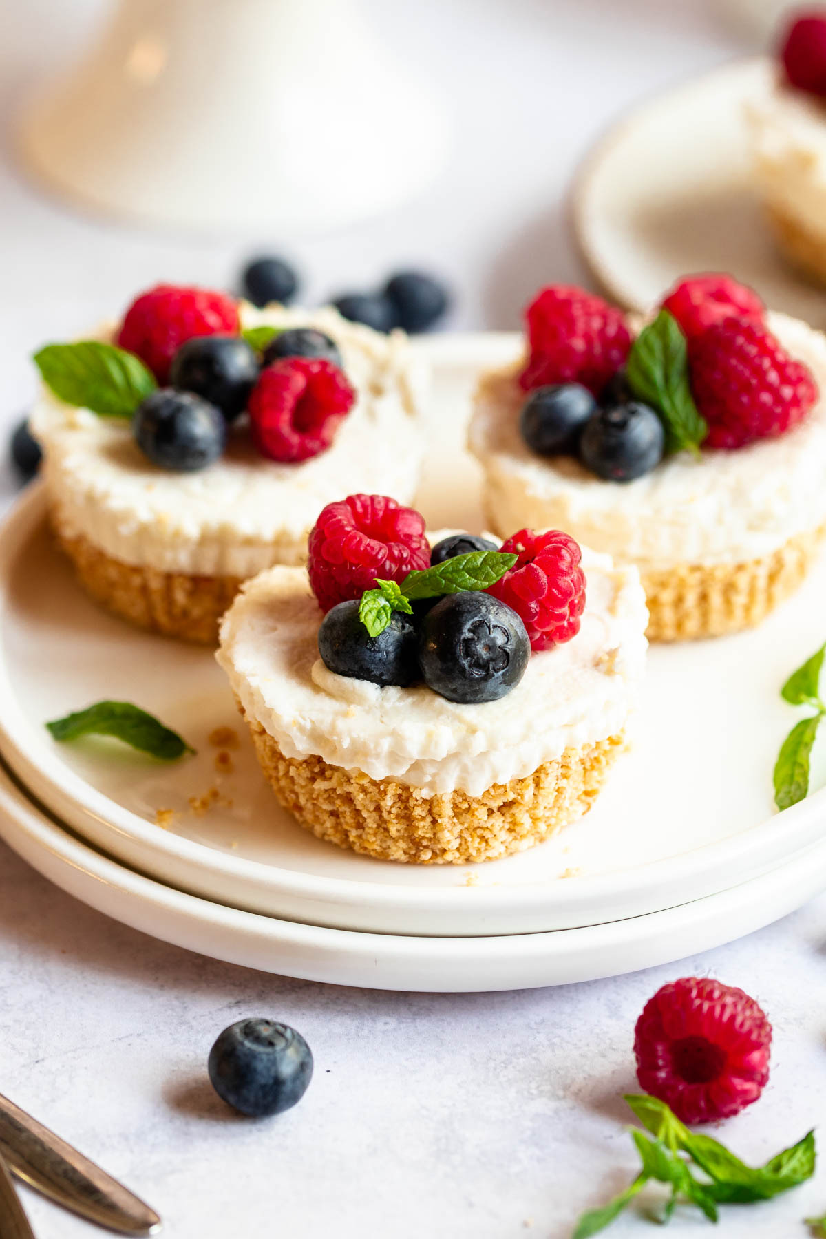 Three mini cheesecakes on a white plate with berries on top.