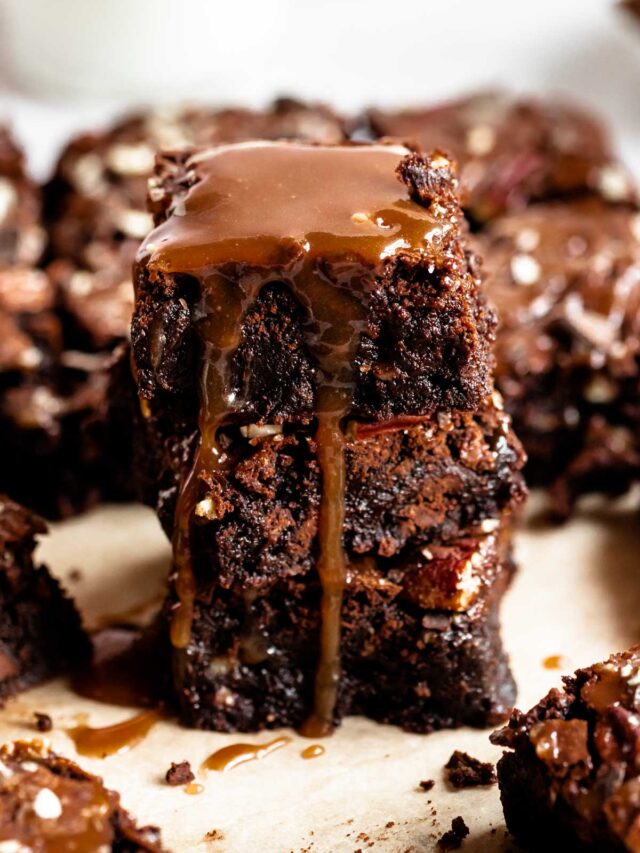 Stack of turtle brownies drizzled with caramel sauce.