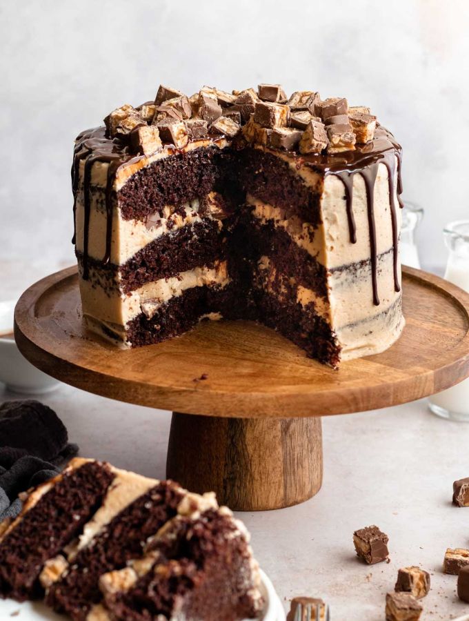 Snickers cake on a wooden cake stand.