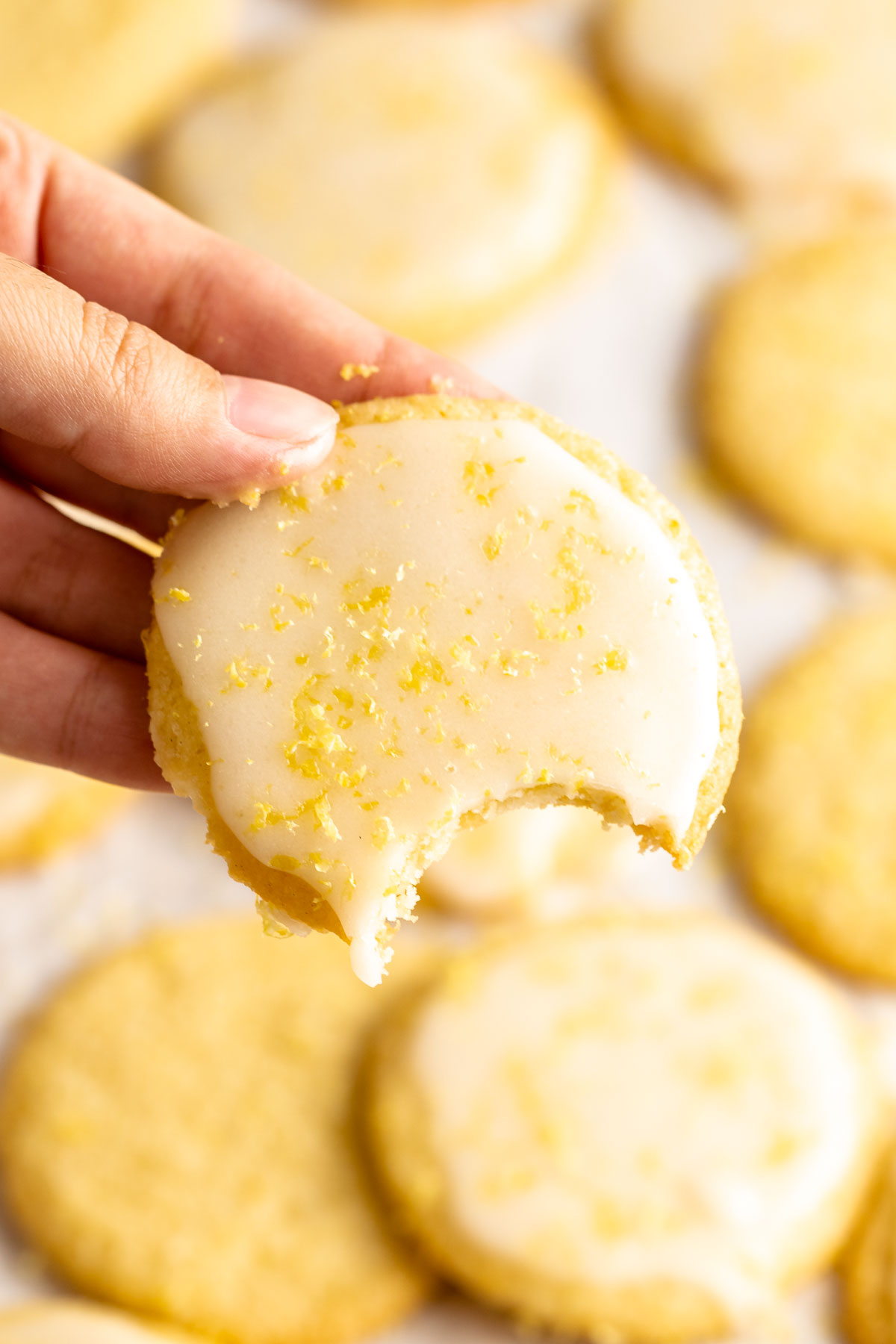 Hand holding a lemon cookie with a bite missing.