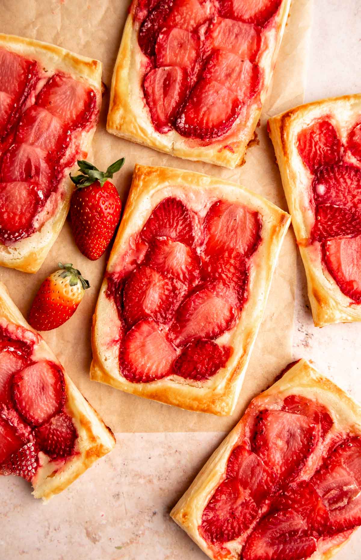 Strawberry danishes on a parchment paper with fresh strawberries.