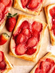 Strawberry danish on a parchment paper with fresh strawberries.