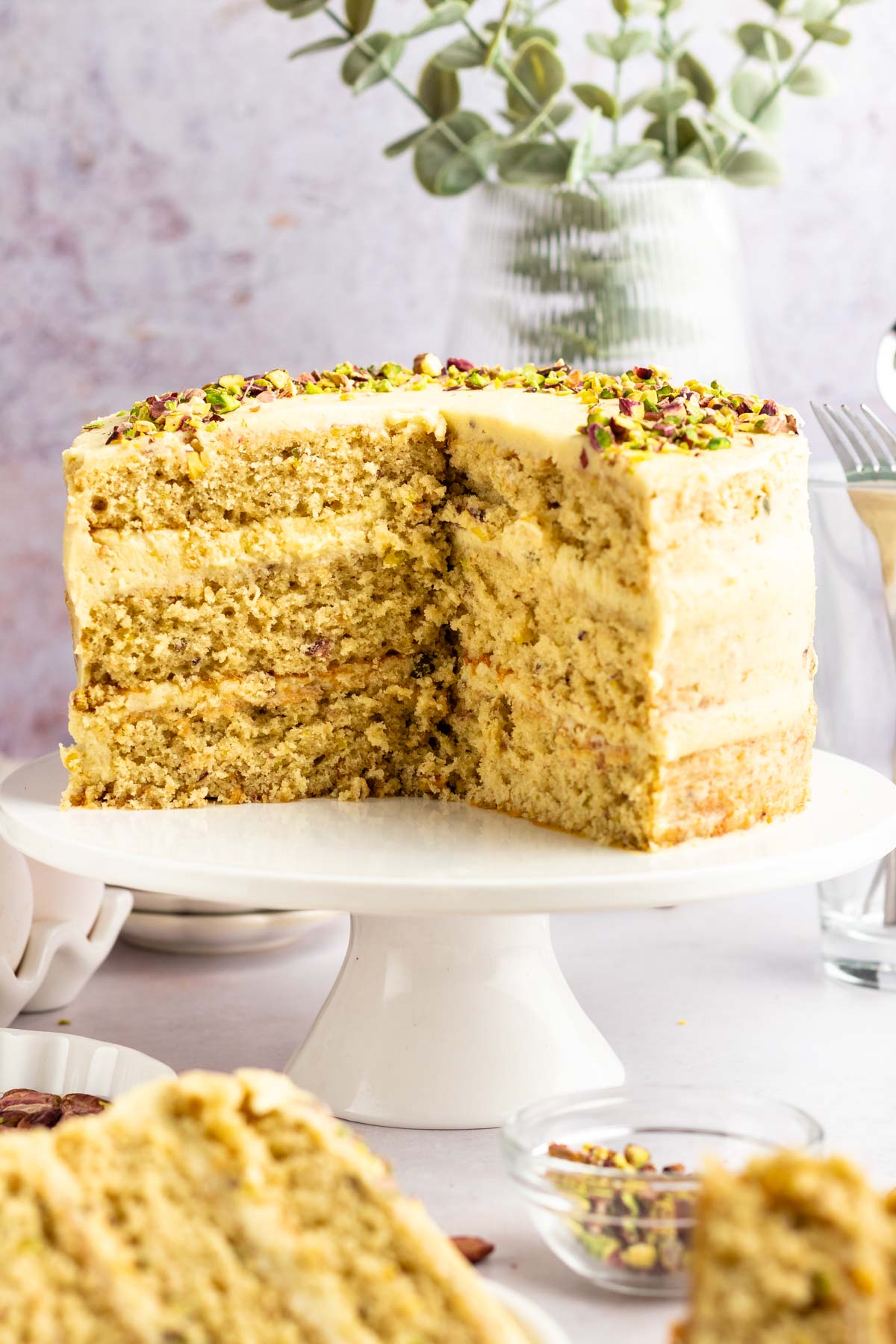 Pistachio cake sliced open on a white cake stand.