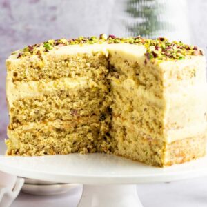 Pistachio cake sliced open on a white cake stand.
