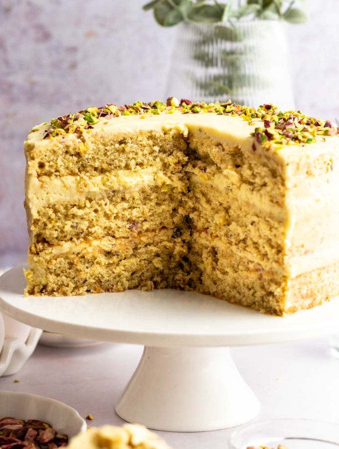 Pistachio cake sliced open on a white cake stand.