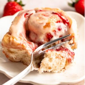 Strawberry cinnamon roll on a plate with a fork.