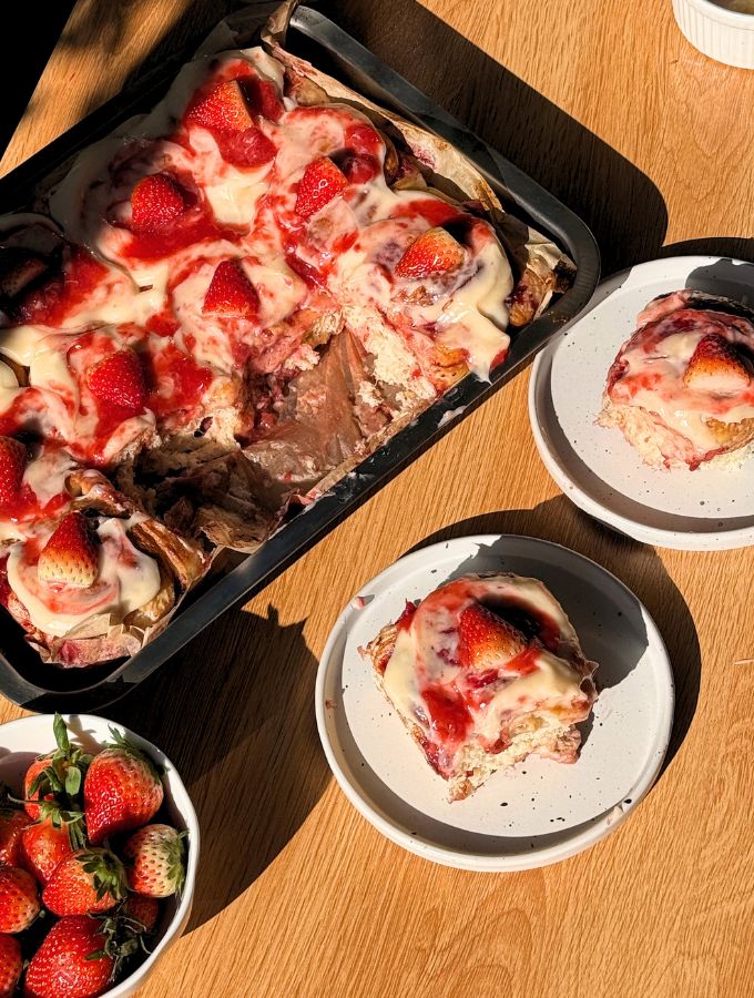 Pan with strawberry cinnamon rolls next to a plate with a roll.