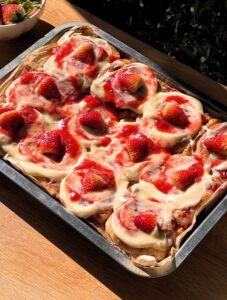 Strawberry cinnamon rolls in a pan with cream cheese frosting on top and strawberries.