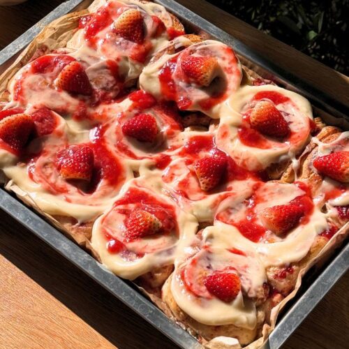 Strawberry cinnamon rolls in a pan with cream cheese frosting on top and strawberries.