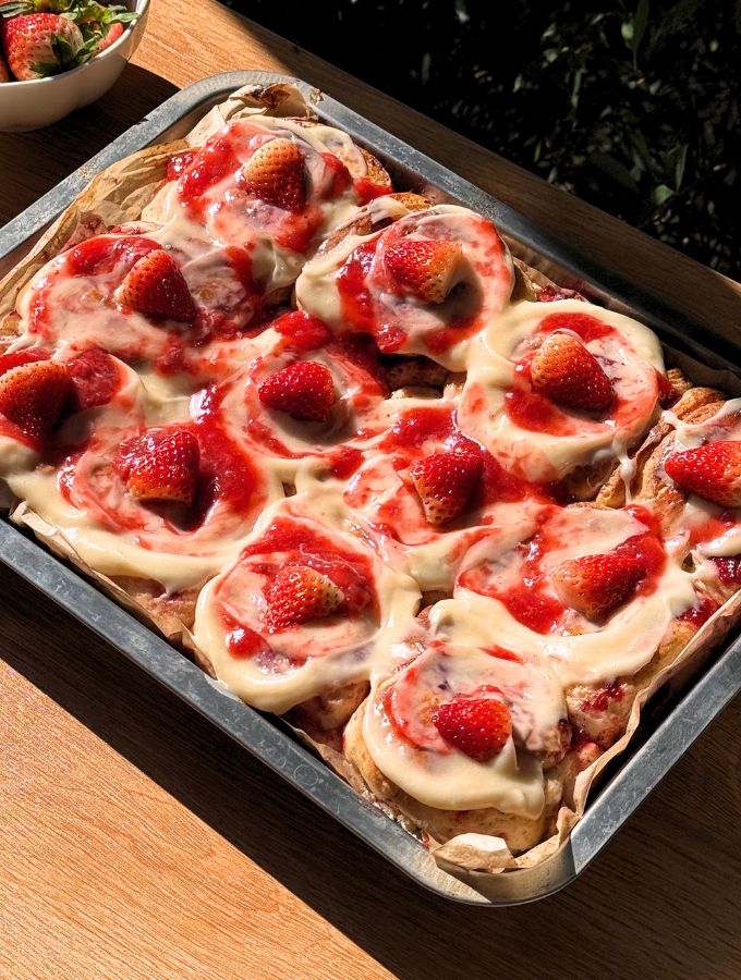 Strawberry cinnamon rolls in a pan with cream cheese frosting on top and strawberries.