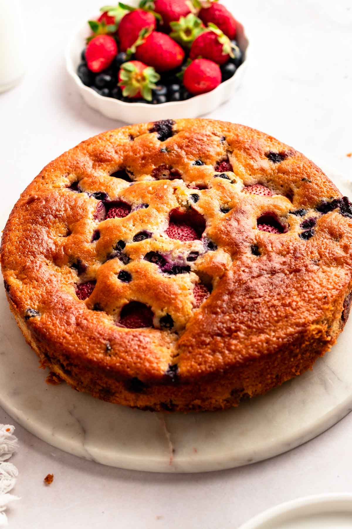 Berry cake on a cake plate next to fresh berries.