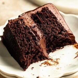 Slice of chocolate ganache cake on a plate with a bite missing.