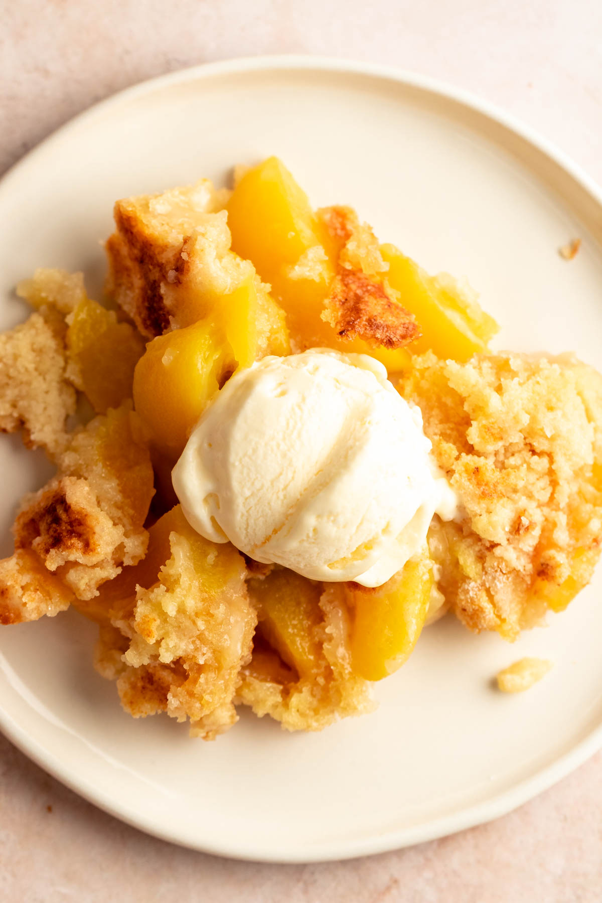 Close up shot of peach cobbler in a white plate with ice cream.