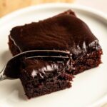 Slice of buttermilk chocolate cake on a white plate with a fork.