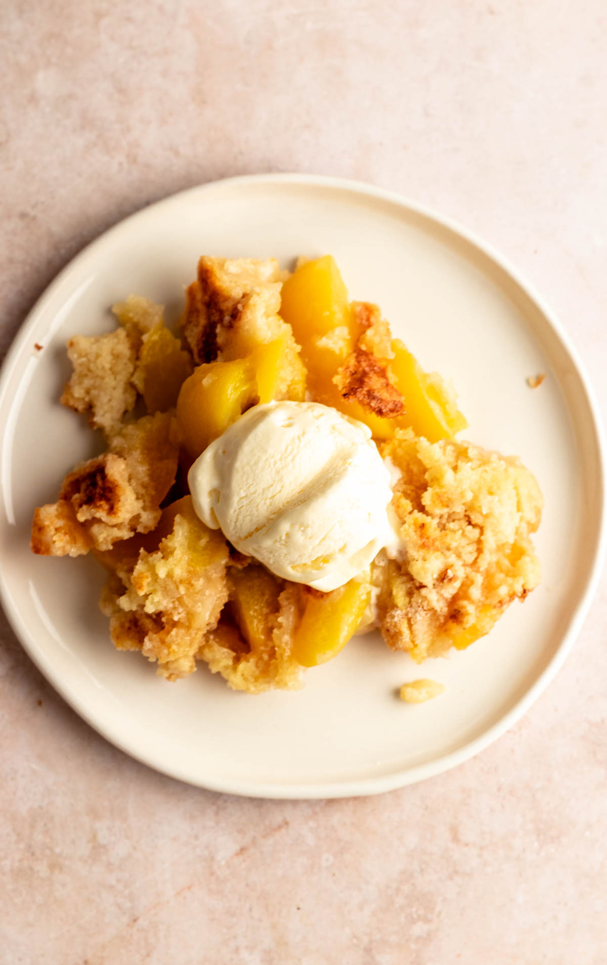 White plate with peach cobbler and vanilla ice cream.