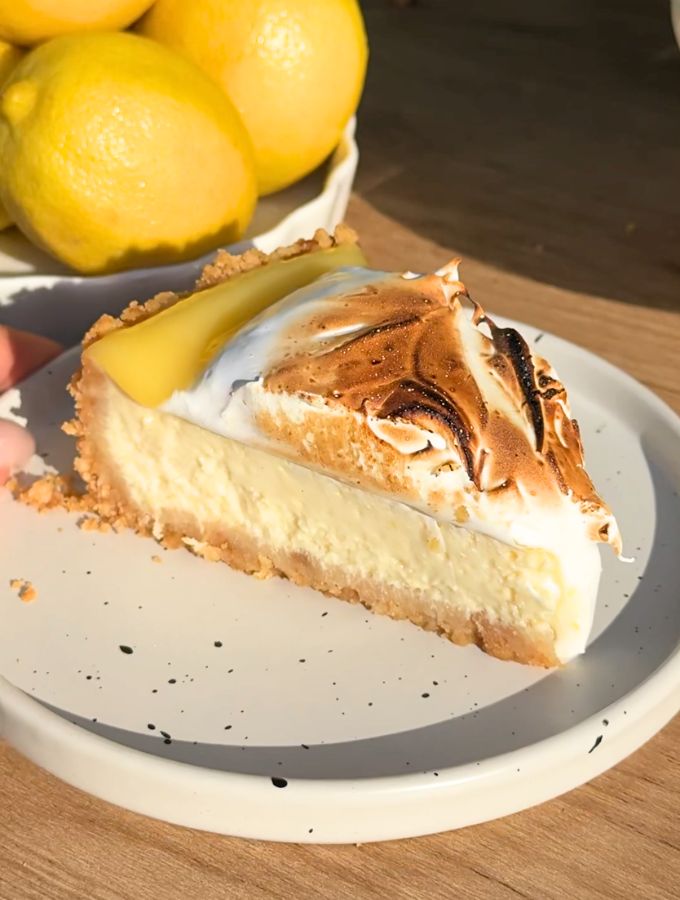 Slice of lemon meringue cheesecake on a white plate.