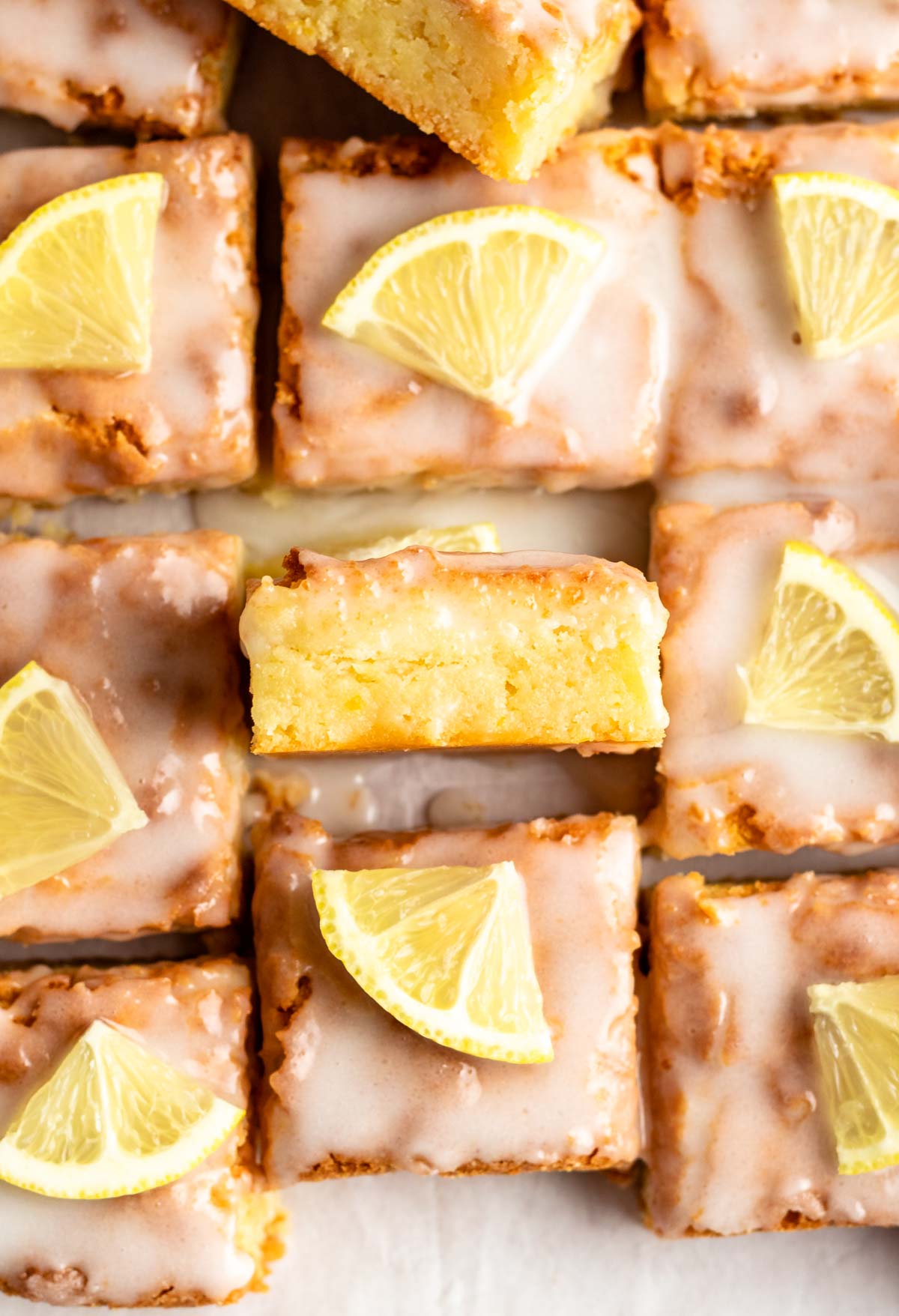 Lemon brownies on a white parchment paper with lemon slices.