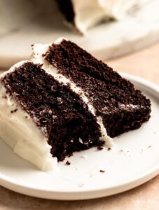 Slice of chocolate cake with cream cheese frosting with a bite missing.