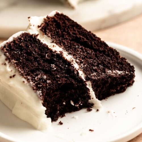 Slice of chocolate cake with cream cheese frosting with a bite missing.