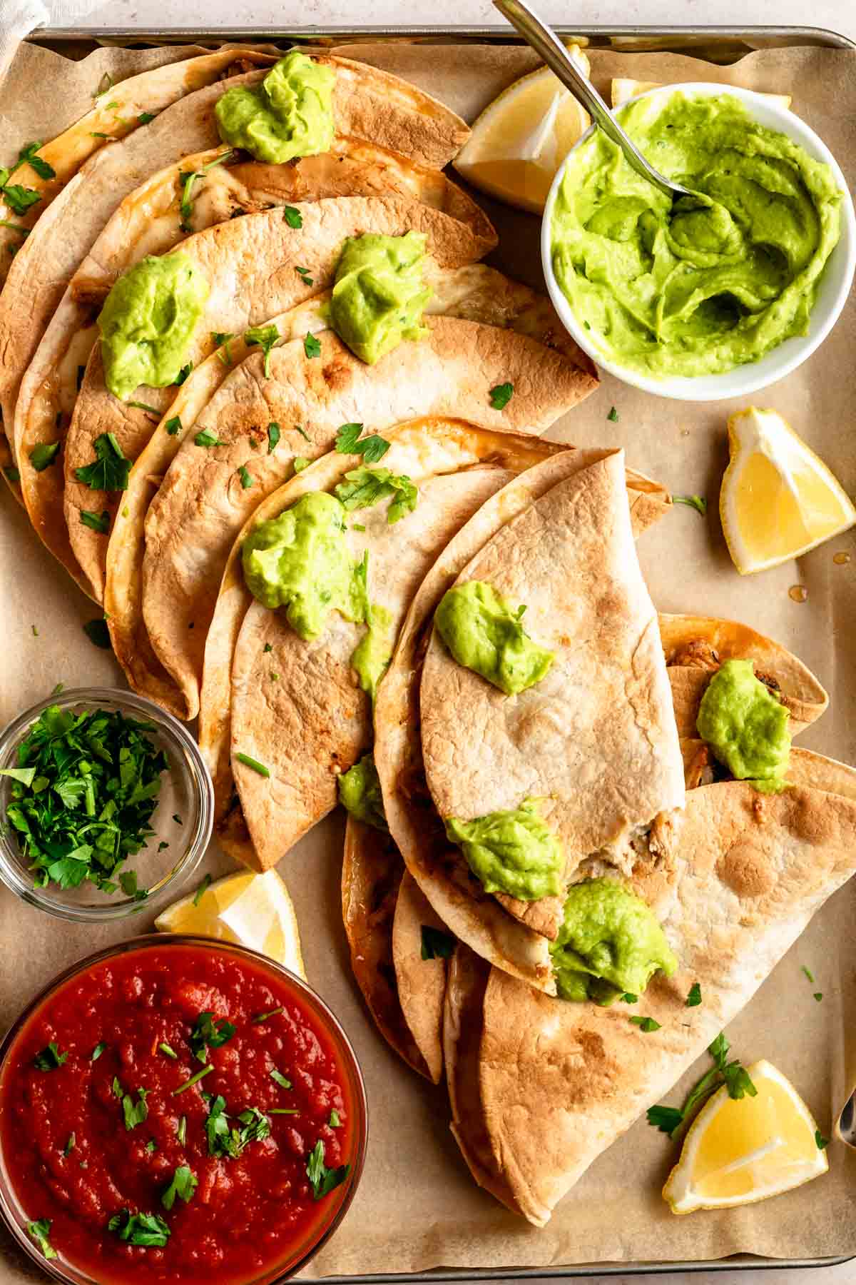 Top of baked chicken tacos next to salsa and avocado sauce.